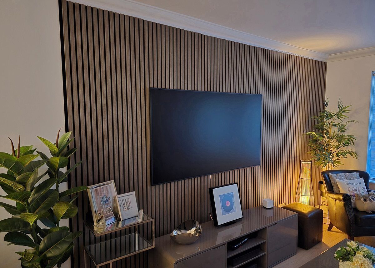 Flat-screen television mounted on a vertical walnut wood slat wall panel with media console.