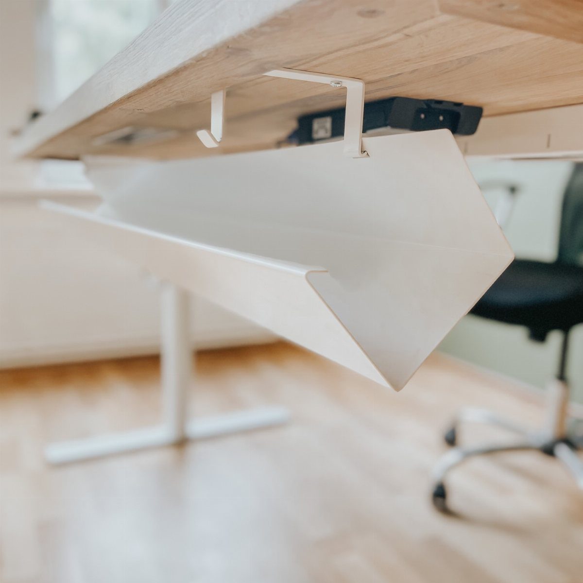 White metal cable tray attached under a wooden desk holding a black power strip.