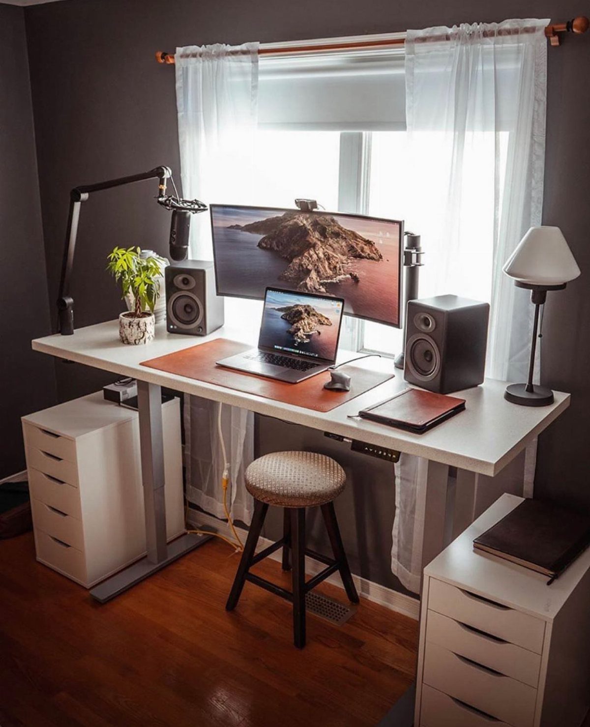White standing desk with computer equipment positioned directly in front of a window.