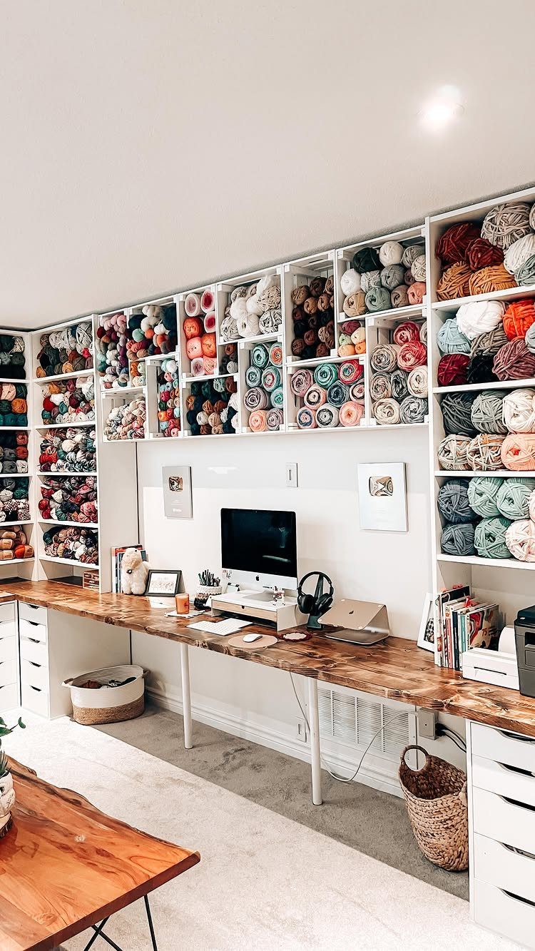Wall-mounted cubby shelves filled with colorful yarn above a long wooden desk.